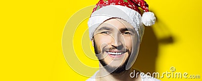 Studio portrait of close male face, smiling man wearing Christmas hat on yellow background with copy space. Stock Photo