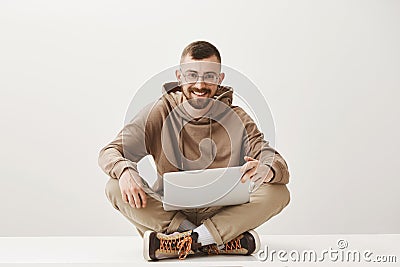 Studio portrait of handsome happy caucasian male with fair hair and beard, wearing glasses sitting on floor with Stock Photo