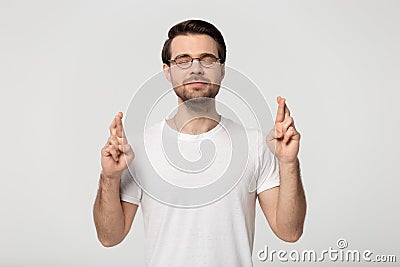 Studio portrait millennial guy in eyeglasses crossing fingers. Stock Photo