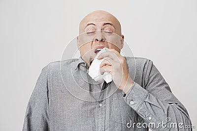 Studio portrait of sick bald caucasian man holding napkin or tissue, trying to cover mouth while sneezing with closed Stock Photo