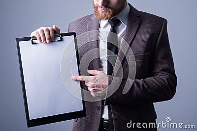 Studio portrait of a young bearded handsome guy of twenty-five years old, in an official suit, holding a folder with a sheet for Stock Photo