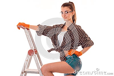 Studio portrait of young beautiful brunette girl in uniform and glasses makes renavation on ladder and smiling on camera Stock Photo