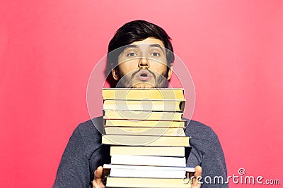 Studio portrait of young guy wearing round eyeglasses with bunch of books in hands on coral pink background. Stock Photo