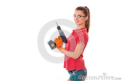 Studio portrait of young brunette girl in uniform and glasses makes renavation with drill in hands smiling on Stock Photo