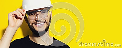 Studio portrait of young smiling construction engineer worker wearing safety helmet and goggles on background of yellow. Stock Photo