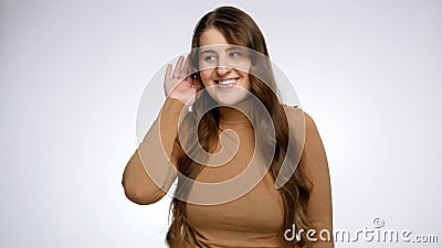 Studio portrait of young woman holding hand near ear and listening. Concept of gossips, getting information and Stock Photo