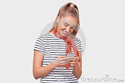 Studio shot of blonde positive smiling young woman using cellphone, messaging to her friend. Happy female chatting with her Stock Photo