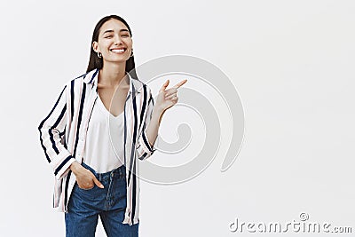 Studio shot of carefree emotive and friendly famous woman in stylish striped blouse, bending and pointing right with Stock Photo