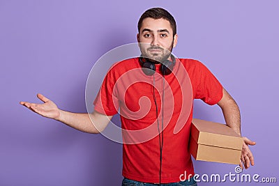 Studio shot of caucasian bearded man dressed red casual t hirt standing isolated over lilac background with carton box in hand, Stock Photo