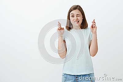 Studio shot of cute excited and hopeful female fan watching important game peeking with one eye and crossing fingers for Stock Photo