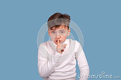 Studio shot of little boy holding his index finger at his lips asking this gesture not to reveal secrets Stock Photo