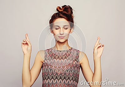 Studio shot of lovely female student has hopeful expression, crosses fingers Stock Photo