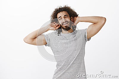 Studio shot of musculine confident hispanic guy with joyful attitude and curly hair, holding hands behind head and Stock Photo