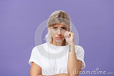 Studio shot of offended sad and timid silly woman with blond hairstyle frowning looking from under forehead holding fist Stock Photo