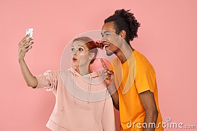 Studio shot of overjoyed dark skinned guy laughs sincerely while poses for selfie with ginger girlfriend, have fun Stock Photo