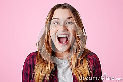 Studio shot of overjoyed happy female laughs at good joke, keeps mouth widely opened, being excited, isolated over pink studio bac Stock Photo