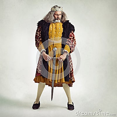 I wield a long sword. Studio shot of a richly garbed king holding a sword suggestively. Stock Photo