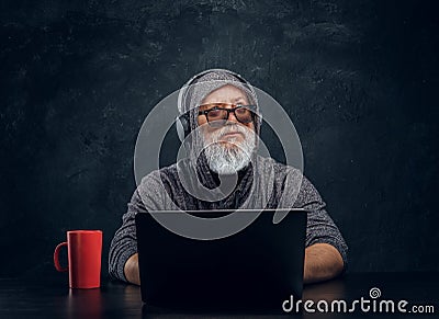 Contemporary elderly hacker with cup and laptop sitting at table Stock Photo