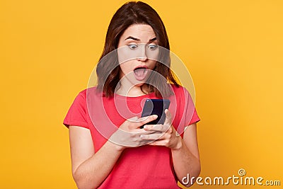 Studio shot of stupefied Caucasian brunette woman posing with widely open mouth, reads incredible news in Internet or shocking Stock Photo