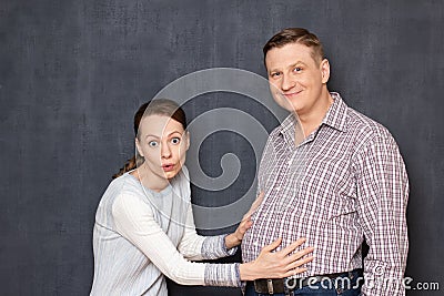 Studio shot of surprised woman touching big stomach of happy man Stock Photo