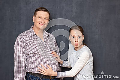 Studio shot of surprised woman touching big stomach of happy man Stock Photo