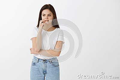 Studio shot of troubled worried beautiful female in trendy clothes, biting lip and fingernail, looking down while Stock Photo