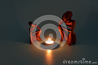 two wooden figurines sitting by a glowing fire of a candle like it was campfire on blue background Stock Photo