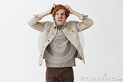 Studio shot of weird funny and panicking redhead guy with beard making faces scratching head insane shouting while Stock Photo