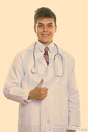 Studio shot of young happy man doctor smiling while giving thumb up Stock Photo