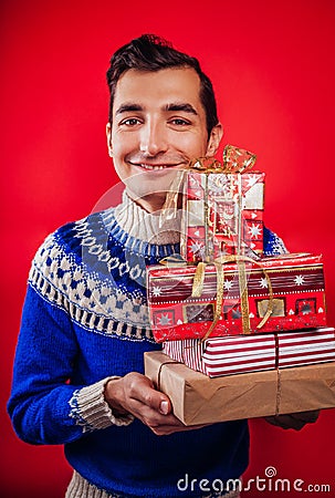 Studio shot of a young man in Icelandic sweater holding a heap of gift boxes. Christmas or New Year celebration concept. Stock Photo