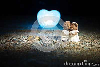 Stuffed bride and groom bears standing together with LED heart on dark foggy background. Stock Photo