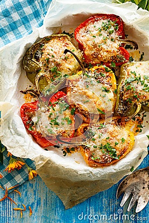 Stuffed peppers, halves of peppers stuffed with bulgur, dried tomatoes, herbs and cheese in a baking dish on a blue wooden table, Stock Photo