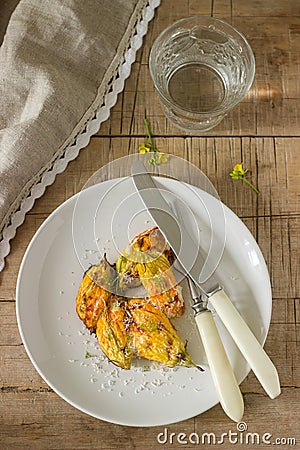 Stuffed with ricotta and cheese baked zucchini and pumpkin flowers served with a glass of mineral water. Rutik style. Stock Photo