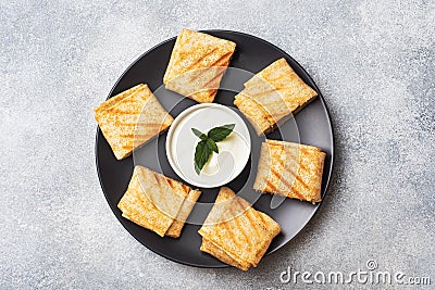 Stuffed thin pancakes rolled into rolls are grilled on a black plate. Cream sauce with mint leaves. Copy space Stock Photo