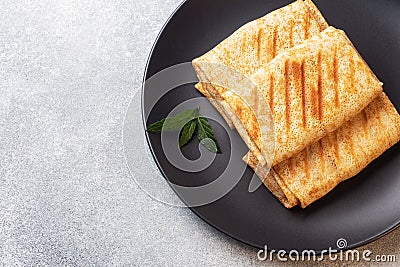 Stuffed thin pancakes rolled into rolls are grilled on a black plate with mint. Copy space Stock Photo
