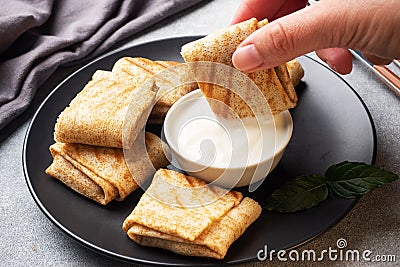 Stuffed thin pancakes rolled into rolls are grilled on a black plate. Pancake roll is dipped in cream sauce. Stock Photo