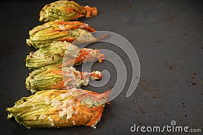 stuffed zucchini or courgette flowers in a row baked with parmesan cheese on a dark baking tray, copy space Stock Photo