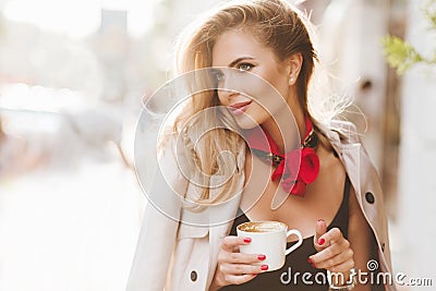 Stunning blonde lady with red neckerchief enjoying good day and driking tasty latte. Outdoor portrait of glad Stock Photo