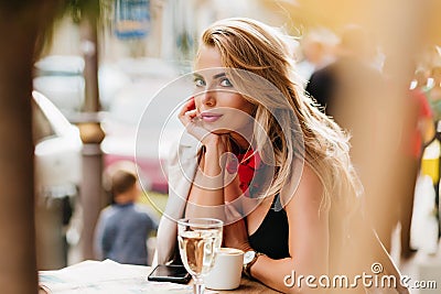 Stunning blonde woman with elegant hairstyle propping face with hand and looking to camera while resting in cafe. Fair Stock Photo