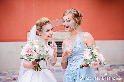 Stunning bride and bridesmaid in blue dress have fun posing before an orange wall Stock Photo