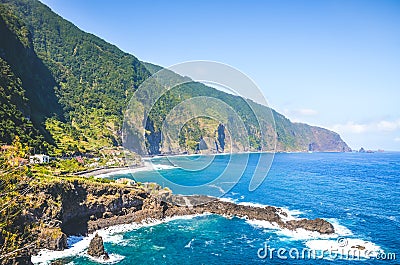Stunning cliffs on the northern coast of Madeira Island, Portugal. Steep green rocks, small city and dark blue sea water Stock Photo