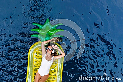 Stunning european woman in swimsuit lying on pineapple mattress. Adorable slim girl in sunglasses c Stock Photo