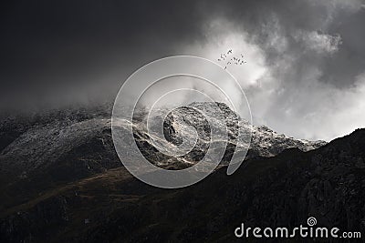 Stunning moody dramatic Winter landscape image of snowcapped Tryfan mountain in Snowdonia with stormy weather brooding overhead Stock Photo