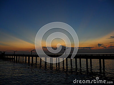 Stunning orange yellow after glow on dark blue sunset sky over the bridge to the sea Stock Photo