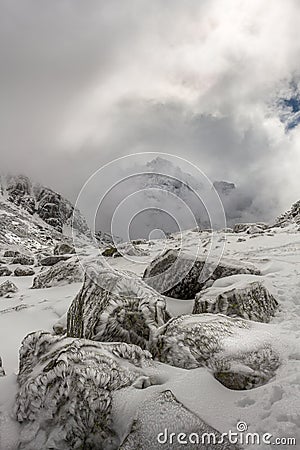 Stunning peak in the clouds and beautiful ice flowers on the rocks after a winter storm at the Rila mountain in Bulgaria, Stock Photo