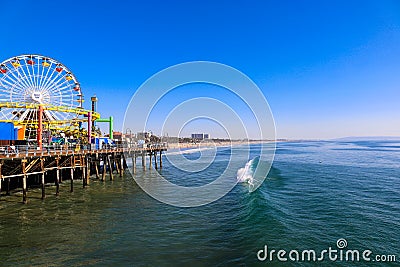 A stunning shot of a colorful Ferris wheel, rollercoaster and carnival games on a long brown wooden pier Editorial Stock Photo