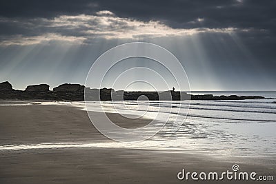 Stunning sun rays bursting from sky over empty yellow sand beach Stock Photo