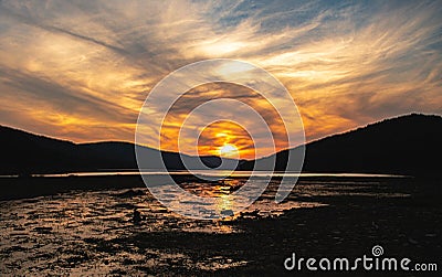 Stunning sunset casts a beautiful orange and pink hue across the water of a marshy estuary Stock Photo
