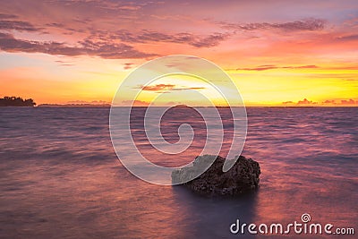 A stunning sunset or sunrise skies with smooth blurry water on Harapan Island, Indonesia. A rock with beautiful magenta skies on Stock Photo