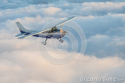 Stunning view of a blue and white little private Cessna airplane browsing the sky over fluffy fairy tale clouds. Stock Photo